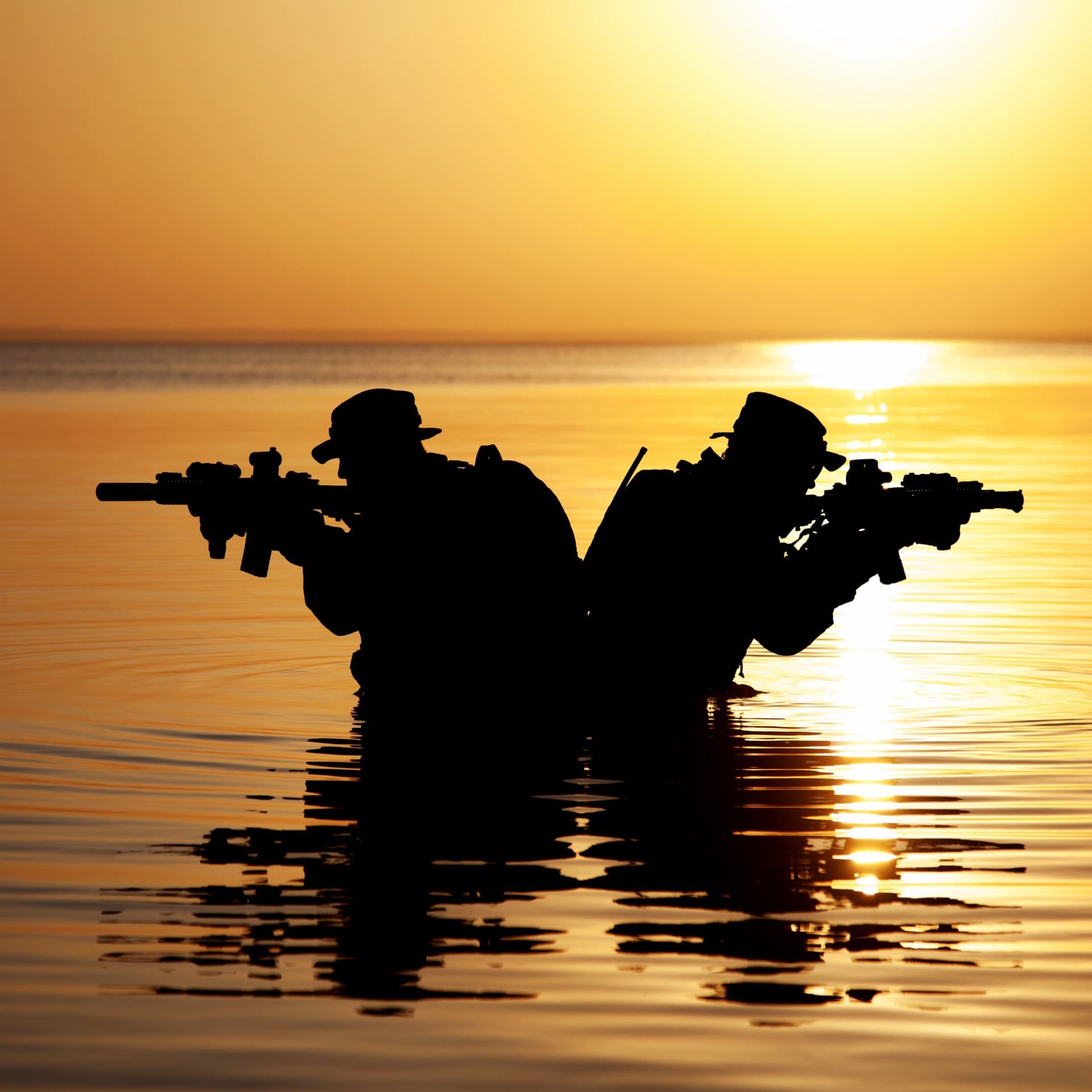 Silhouetted patrol wading through water at sunset